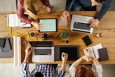 Four professionals sitting around a table with their computers, notes, and devices, showing an example of how IronBridge Private Wealth partners with CPAs and legal counsel to coordinate the client's financial plan.